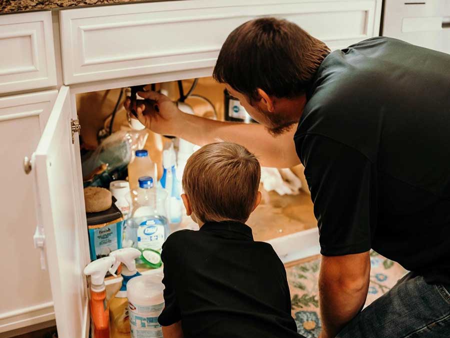 Father checking under-sink plumbing with a child during home plumbing maintenance