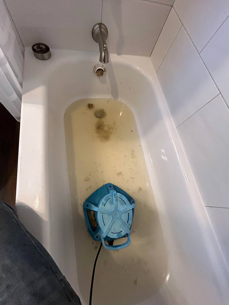 Bathtub drain cleaning in progress with a cable machine clearing a clog